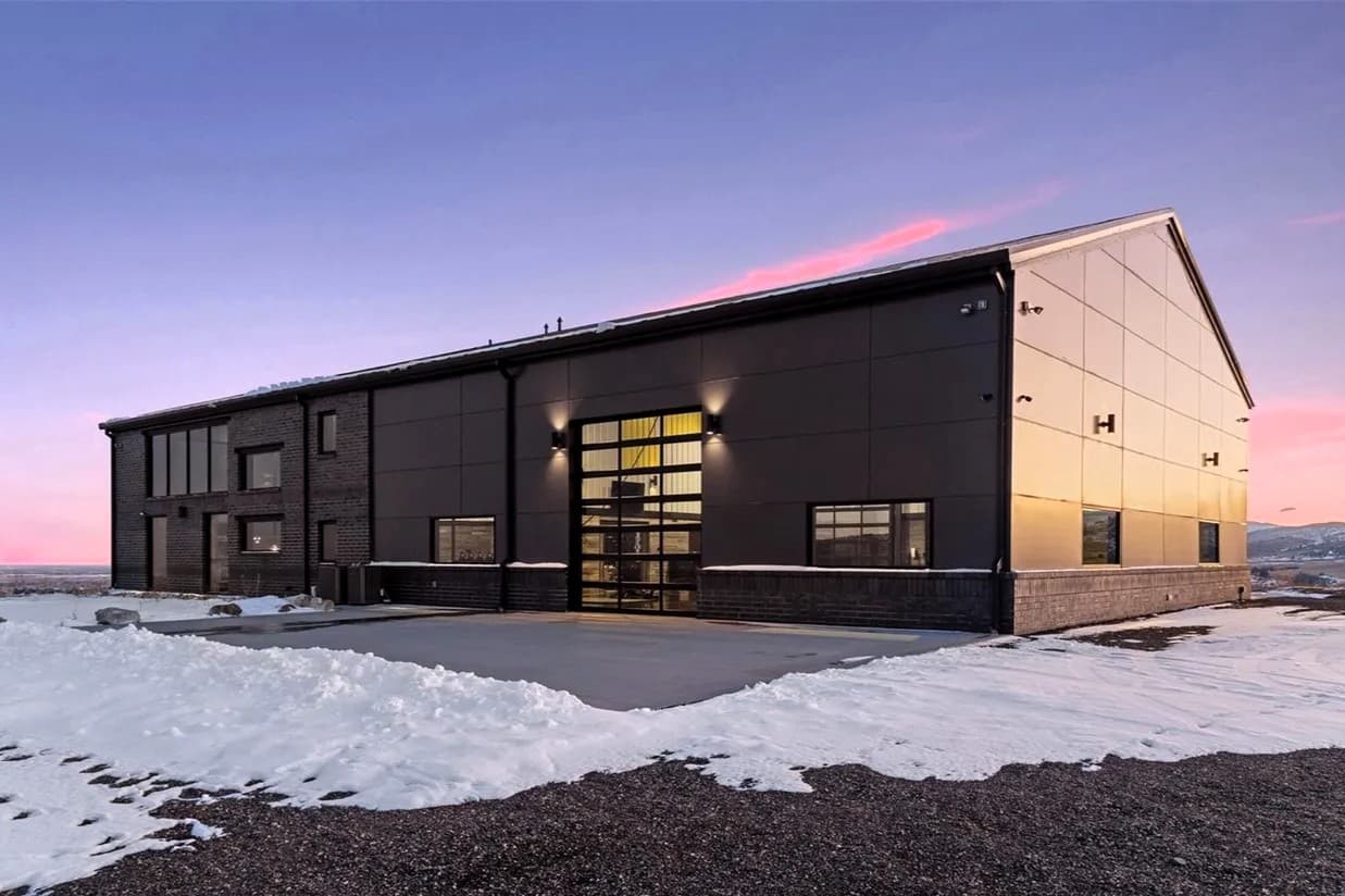 Large dark steel gable building with brick accents at sunset