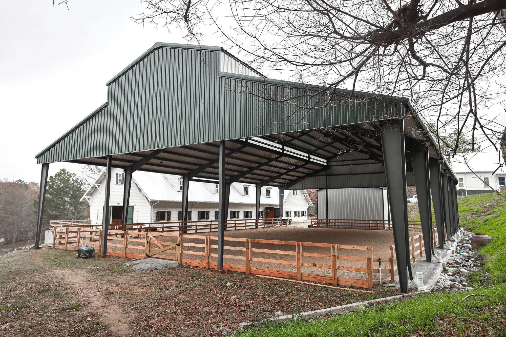 Steel covered riding arena with barn and wood fencing