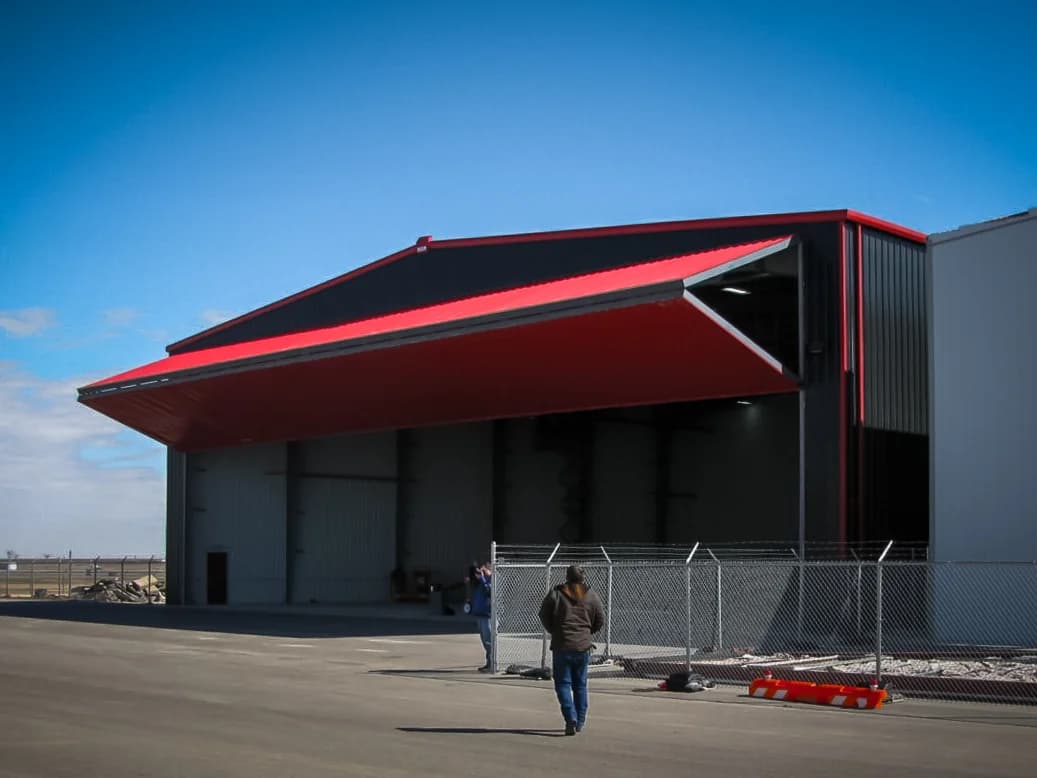Steel hangar with red bifold door and person for scale