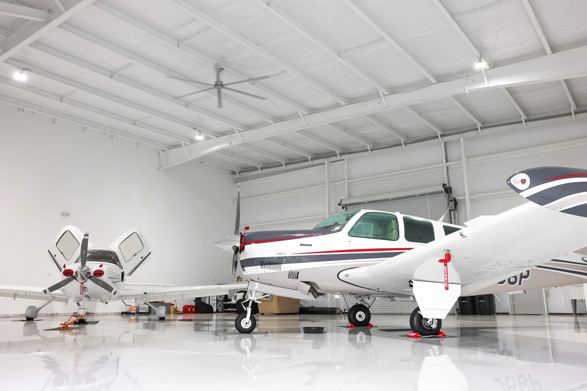 Multiple aircraft stored in clear-span steel hangar with insulated ceiling and HVLS fan